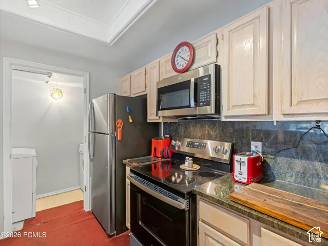 Kitchen featuring stainless steel appliances, wood-finish cabinetry, dark stone countertops, a matching dark stone backsplash, and recessed ceiling lighting