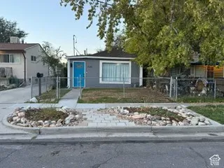 Gray exterior with a blue entry door, concrete walkway, and chain-link fencing