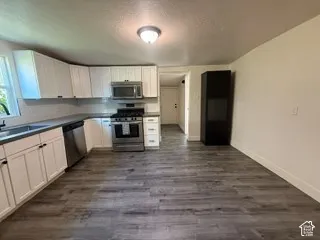 Kitchen featuring white shaker cabinetry, stainless steel appliances, dark countertops, and wood-finish flooring