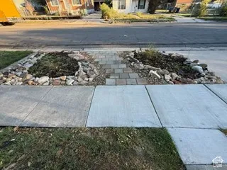 Manicured front yard with paver stone walkway, decorative rock beds, and concrete sidewalk