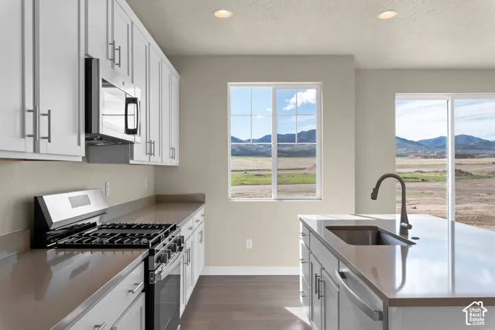 Kitchen featuring white cabinetry, stainless steel appliances, a center island with an integrated sink, and durable countertops