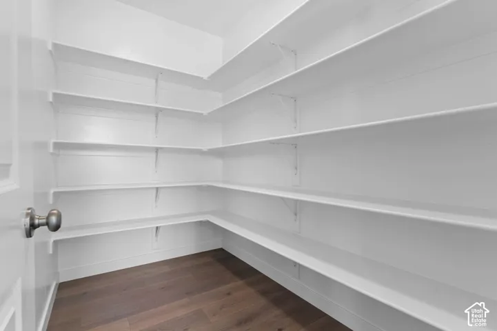 Walk-in pantry with extensive shelving, white finishes, and wood-finish flooring