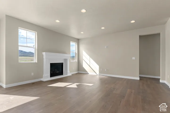 Living area featuring wood-finish flooring, a white mantel fireplace, multiple windows, recessed lighting, and neutral wall tones