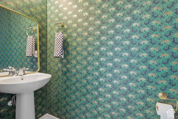 Pedestal sink with chrome faucet, gold-framed mirror, and cute animal patterned wallpaper