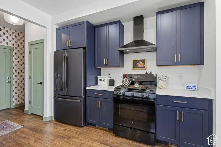 Kitchen featuring wood-finish flooring, dark blue cabinetry, black stainless steel refrigerator, black range, and white quartz countertops