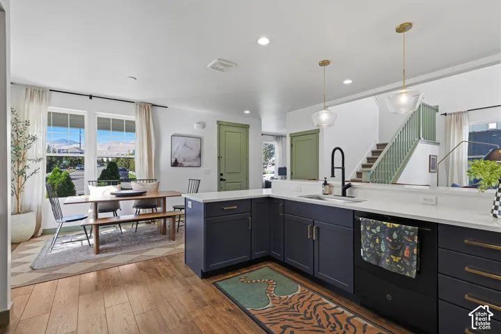 Kitchen featuring bright cabinetry, quartz countertops, wood-finish flooring, a built-in sink with a matte black faucet, and pendant lighting