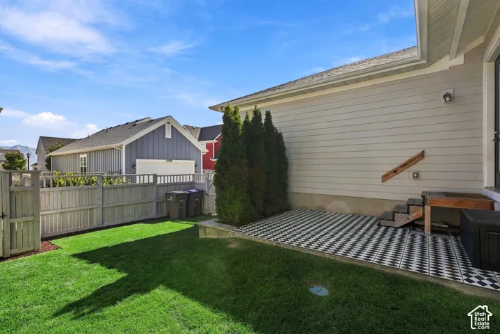 Manicured lawn with a wooden privacy fence, leading to a checkered patio with rear entry into house