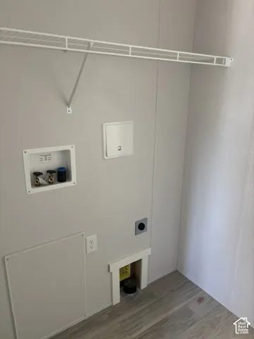 Laundry area featuring a wire storage shelf, utility hookups, and wood-finish flooring