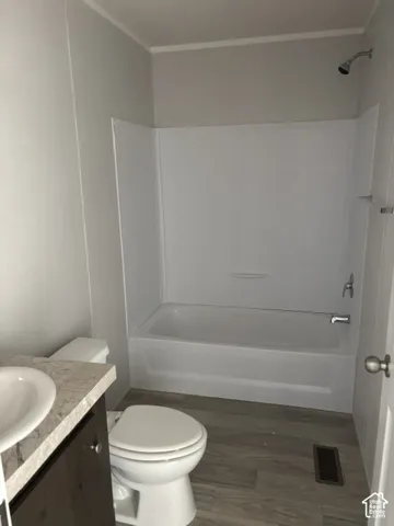 Bathroom featuring a white tub/shower combination, a vanity with a light-toned countertop and integrated sink, a toilet, and wood-finish flooring