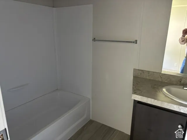 White bathtub with integrated shower surround, dark wood-finish vanity with a single basin sink, and a stone-look countertop