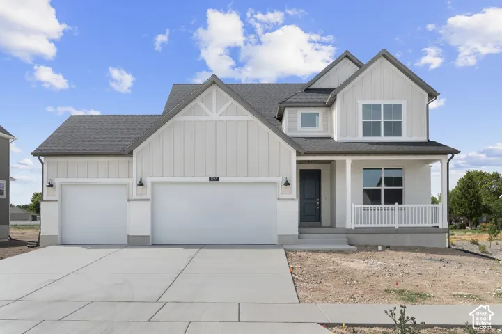 Modern farmhouse exterior with white board and batten siding, dark gray shingle roof, two-car garage, covered porch with white railing, and a dark blue entry door