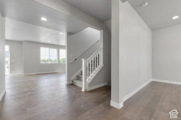 Wood-finish flooring throughout, recessed lighting, white trim, and a carpeted staircase with white balusters