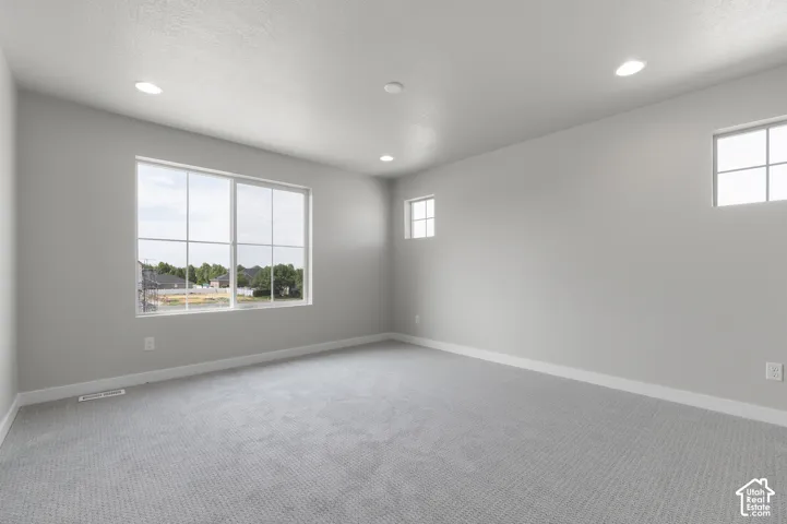 Recessed lighting and multiple windows provide ample illumination in this space featuring light gray walls and textured gray carpeting