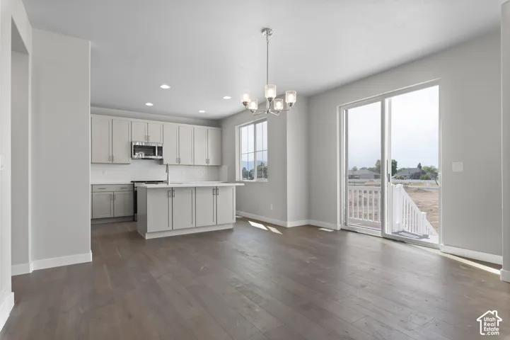 Open-concept living space with wood-finish flooring, a contemporary chandelier, and a kitchen featuring light gray cabinetry