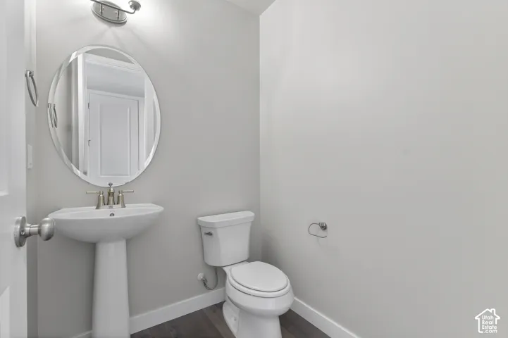 Pedestal sink with brushed nickel faucet, oval mirror, wall-mounted light fixture, and wood-finish flooring