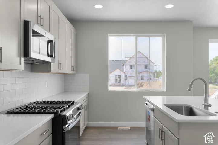 Light-toned cabinetry, stainless steel microwave, gas range, subway tile backsplash, and a kitchen island with an undermount sink