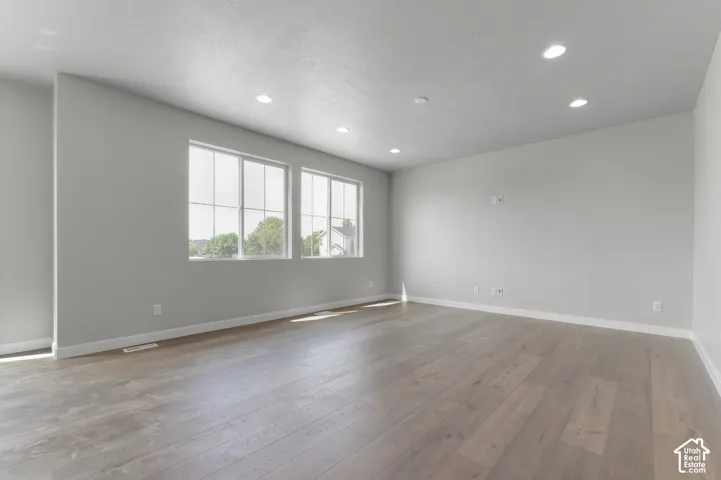 Spacious room featuring light wood-finish flooring, recessed lighting, and multiple windows with white trim