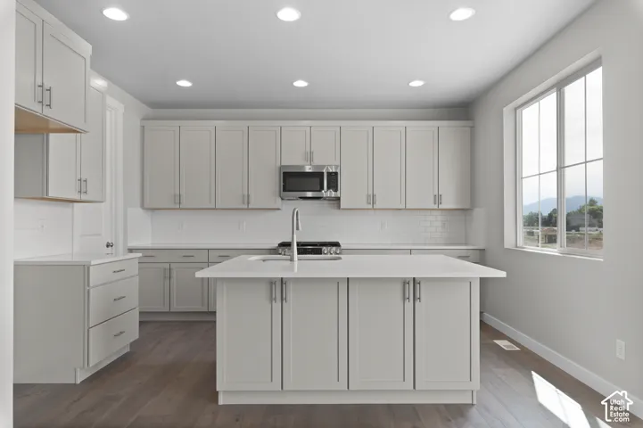 Modern kitchen featuring light gray cabinetry, white subway tile backsplash, recessed lighting, wood-finish flooring, and a central island with an integrated sink