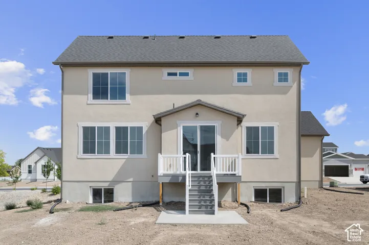 Stucco exterior with a shingled roof, featuring multiple windows, a covered deck, and sliding glass doors