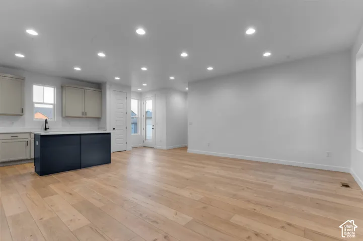 Open-concept living area featuring wood-finish flooring, recessed lighting, a kitchen island with storage, light-colored cabinetry, and a glass-paneled exterior door