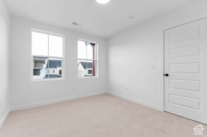 Neutral-toned carpet flooring, two white-framed windows, a white paneled door with a matte black knob, and recessed ceiling lighting