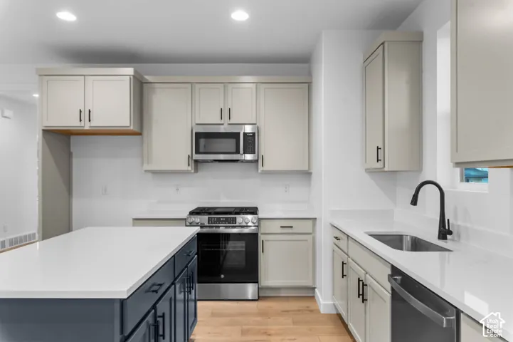 Modern kitchen featuring a two-tone island with a light countertop, stainless steel appliances, a black faucet, and wood-finish flooring