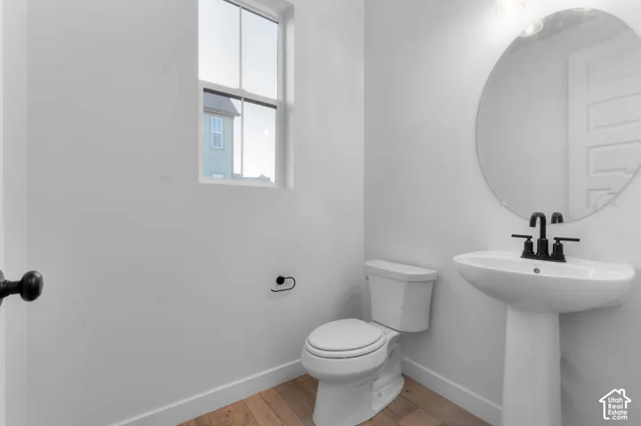 Pedestal sink with a matte black faucet, round mirror, and wood-finish flooring