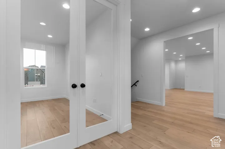 White interior walls, recessed lighting, wood-finish flooring, interior French doors, and a window with white trim