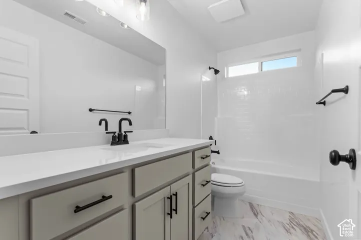 Bathroom featuring a light-toned vanity with dark hardware, a single sink with a matte black faucet, a large mirror, a shower-tub combination with white subway tile, and wood-finish flooring