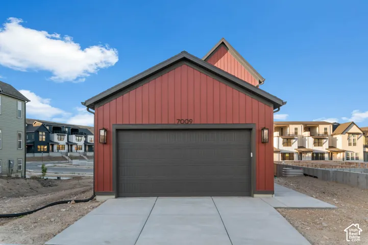 Red vertical siding exterior with dark trim, featuring a dark garage door, two exterior wall sconces, and a concrete driveway