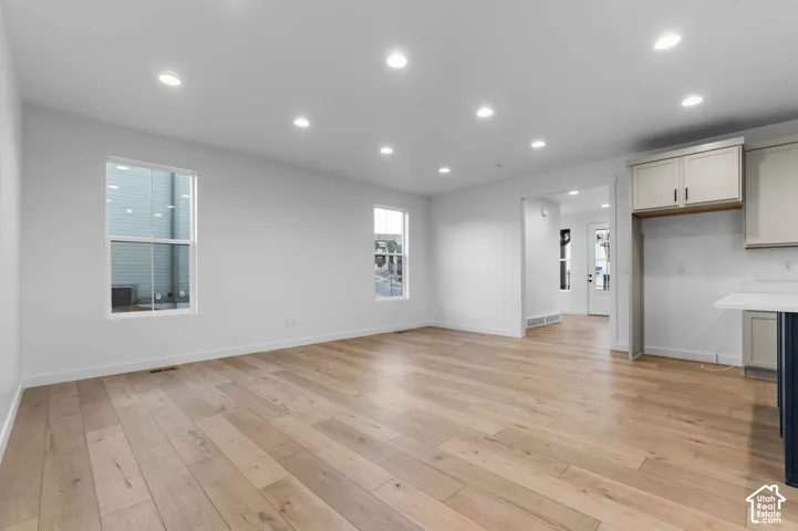 Open concept living area featuring wood-finish flooring, recessed lighting, white walls, and a partial kitchen with white cabinetry and a light-toned countertop