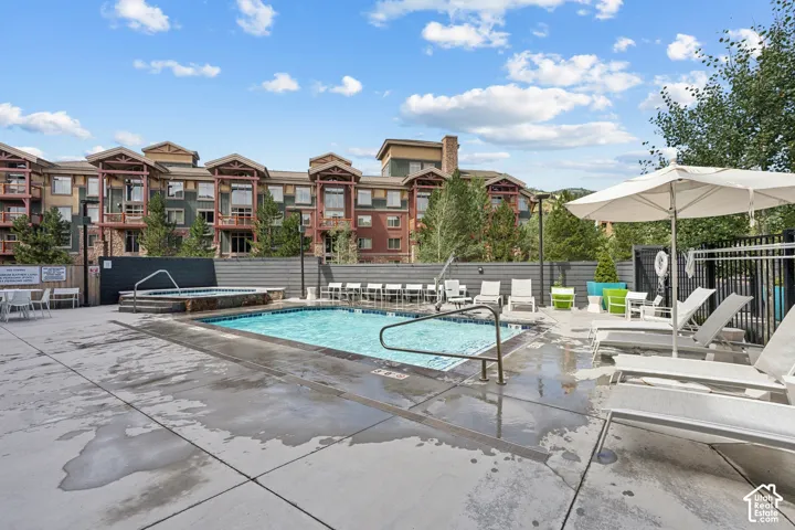 Outdoor pool with an integrated hot tub and surrounding lounge seating, featuring a concrete patio and a privacy fence