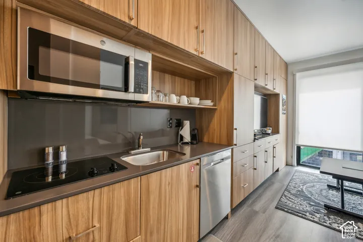 Compact kitchen featuring wood-finish cabinetry, stainless steel appliances, a built-in cooktop, and a stainless steel sink
