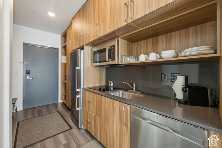 Compact kitchen featuring a stainless steel refrigerator, built-in microwave, integrated dishwasher, and wood-finish cabinetry