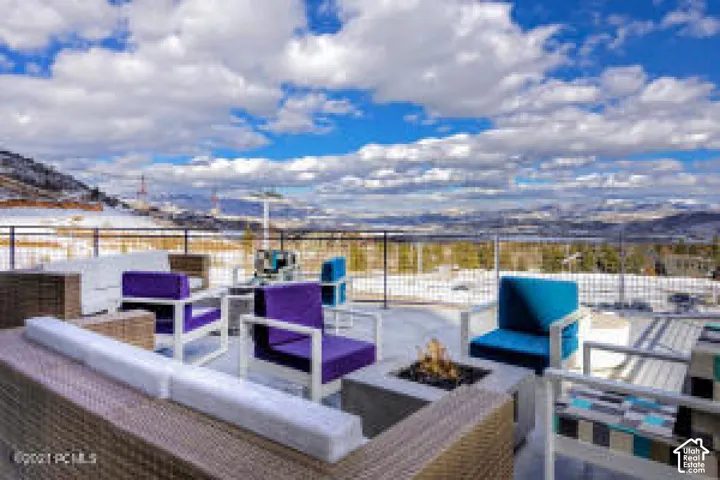 Expansive outdoor terrace with a concrete fire pit, metal railing, and snow-covered distant mountains