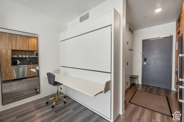 Integrated wall bed with a built-in desk, wood-finish flooring, full-length mirror, and entryway with a modern door
