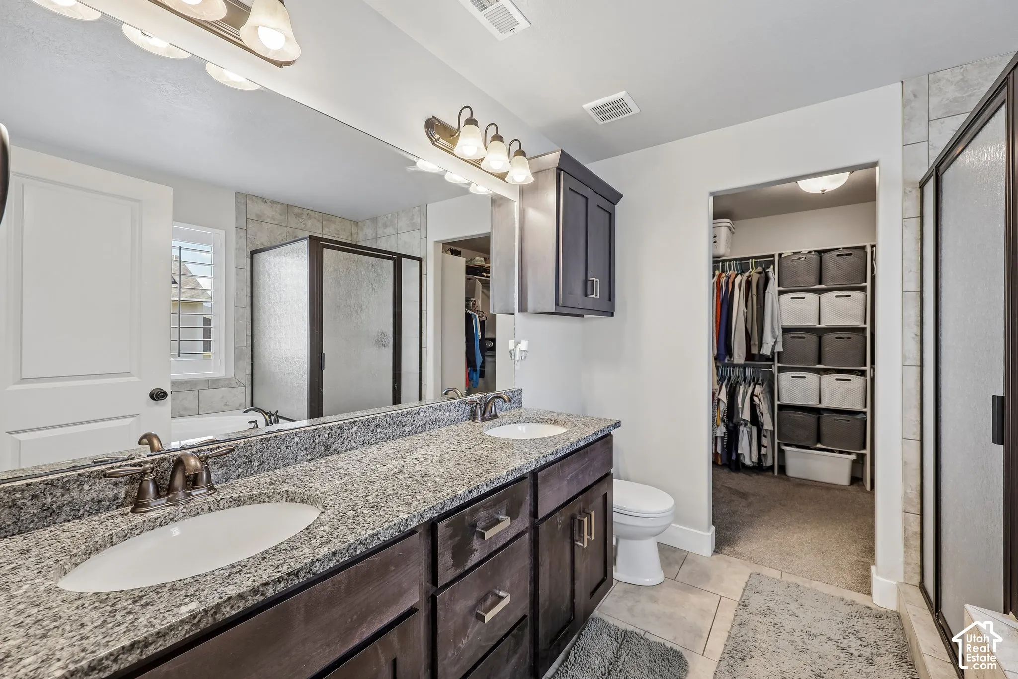 Dual vanity with granite countertop, tiled shower enclosure, separate toilet, built-in storage cabinetry, and an adjacent walk-in closet