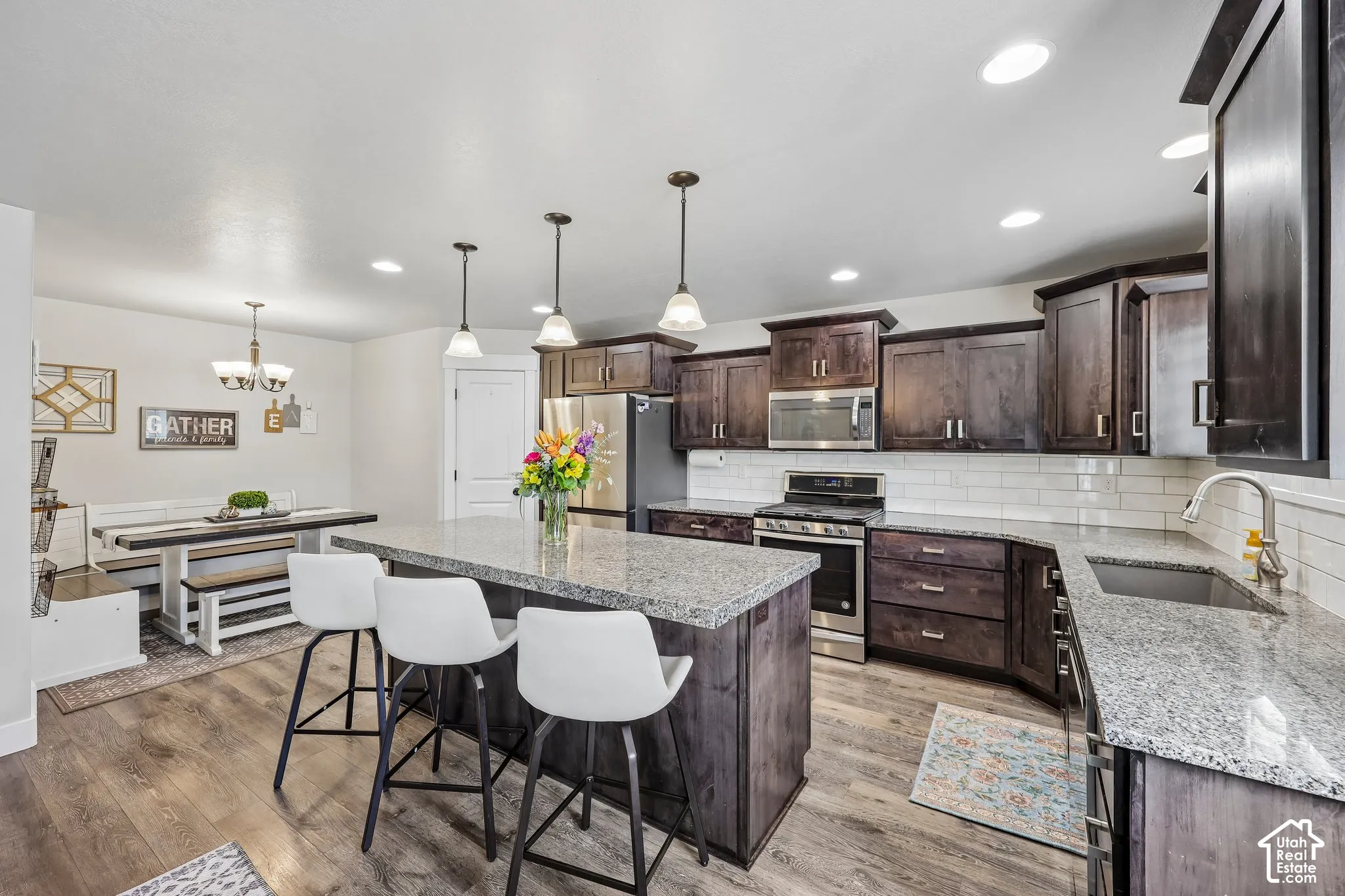 Kitchen featuring an island with pendant lighting, granite countertops, dark wood-finish cabinetry, stainless steel appliances, and wood-finish flooring