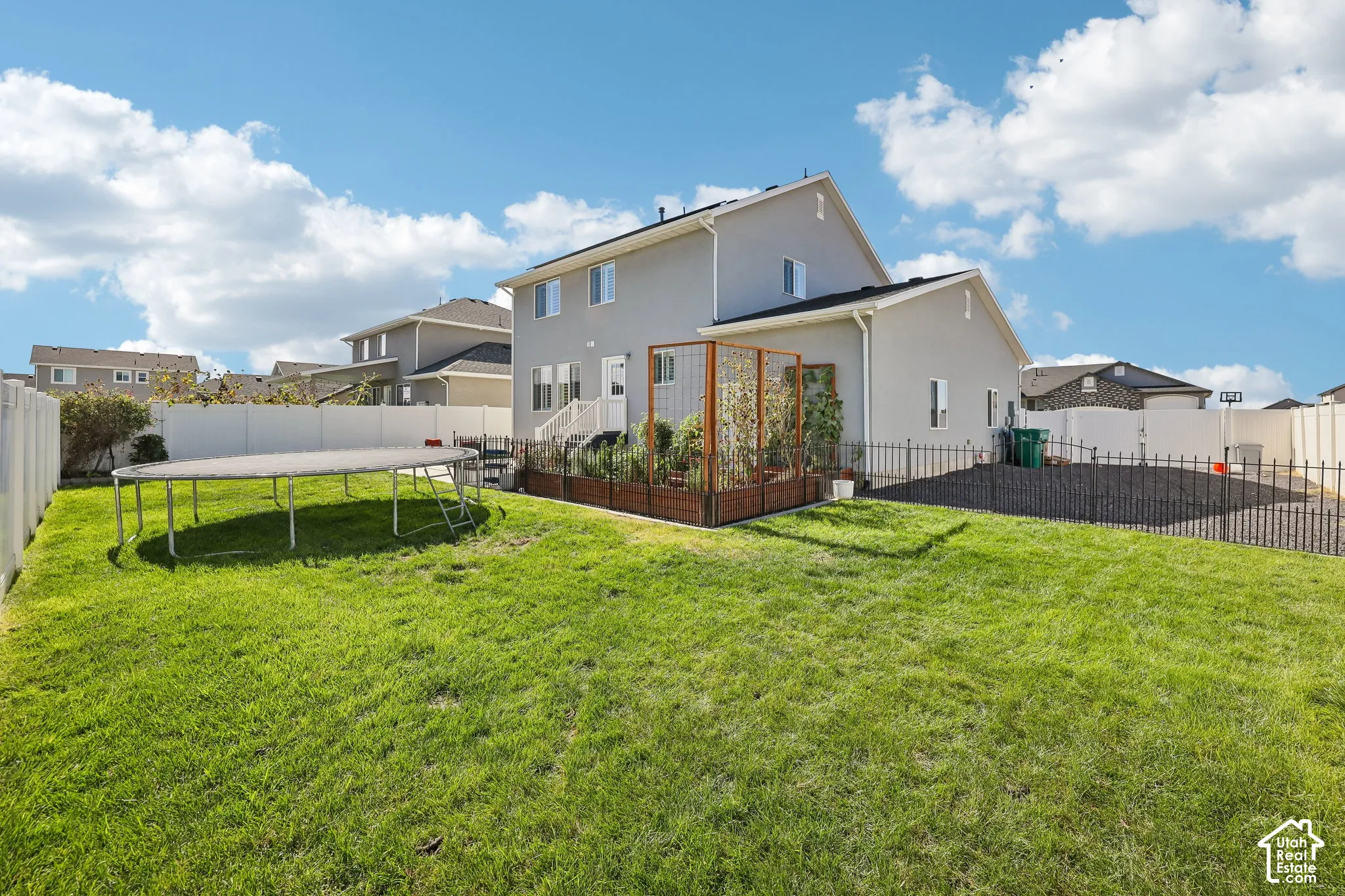 Expansive backyard featuring a manicured lawn, white vinyl fencing, and a dark metal fence