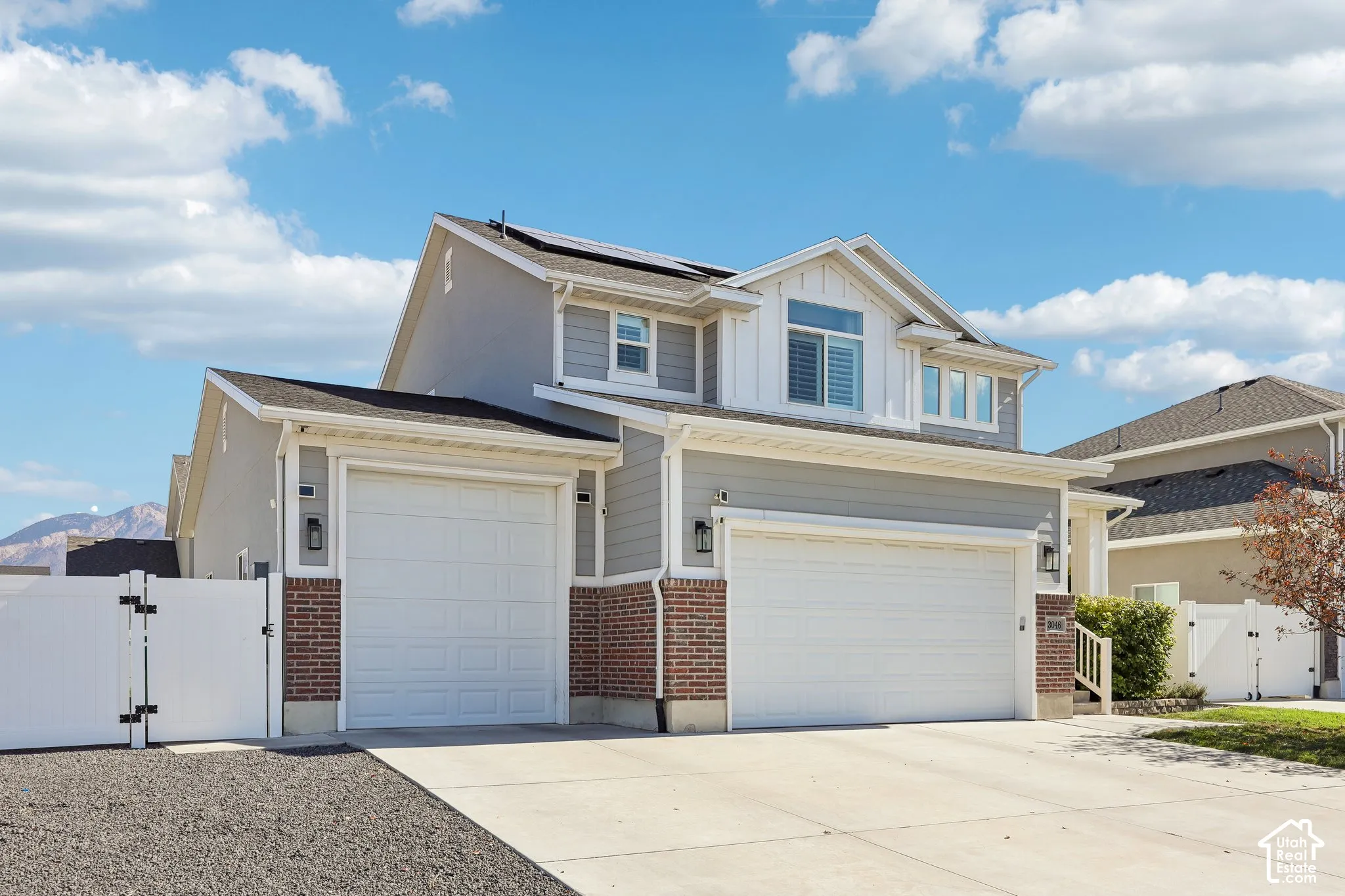 Two-story residence featuring light gray siding with brick accents, multiple garage doors, and solar panels