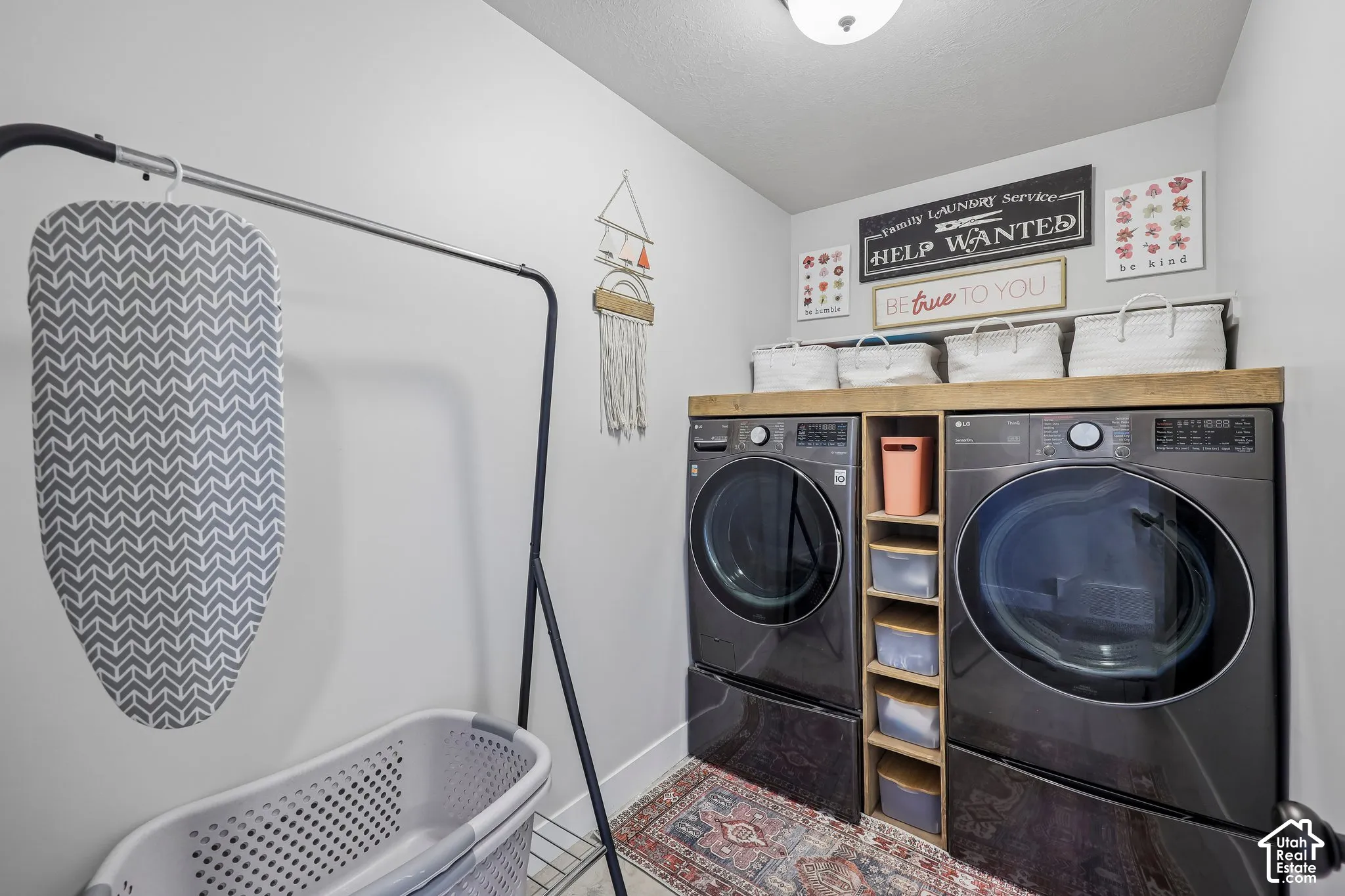 Dedicated laundry room featuring side-by-side front-load washer and dryer with wood-finish cabinetry and open shelving, polished concrete flooring, and bright overhead lighting