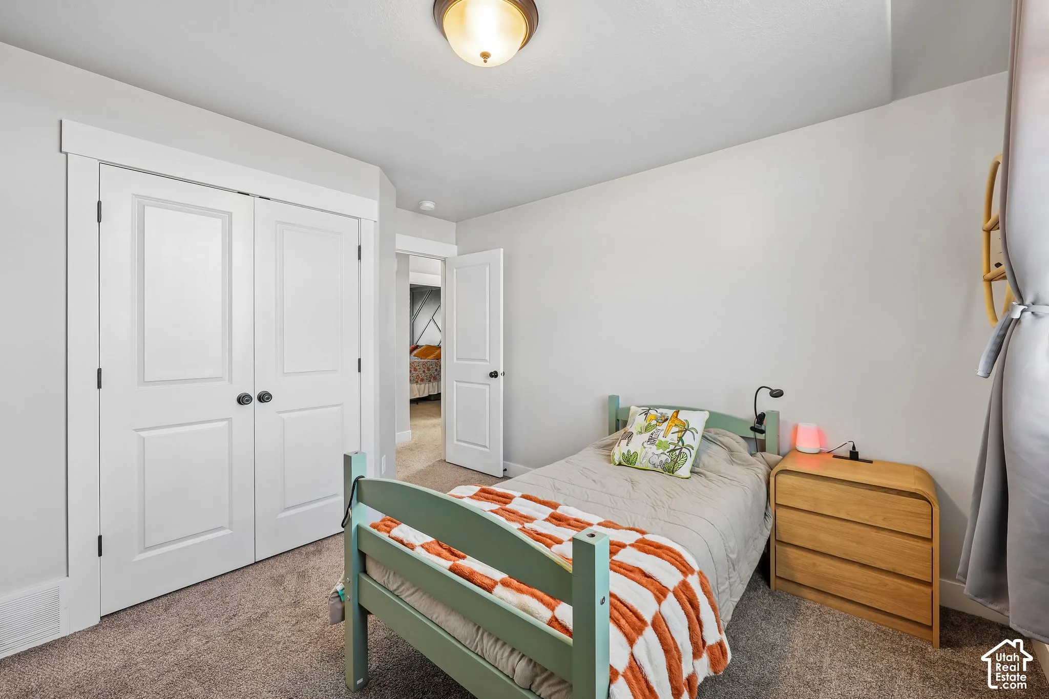 Bright secondary bedroom featuring a green metal bed frame, wood-finish dresser, and carpet flooring