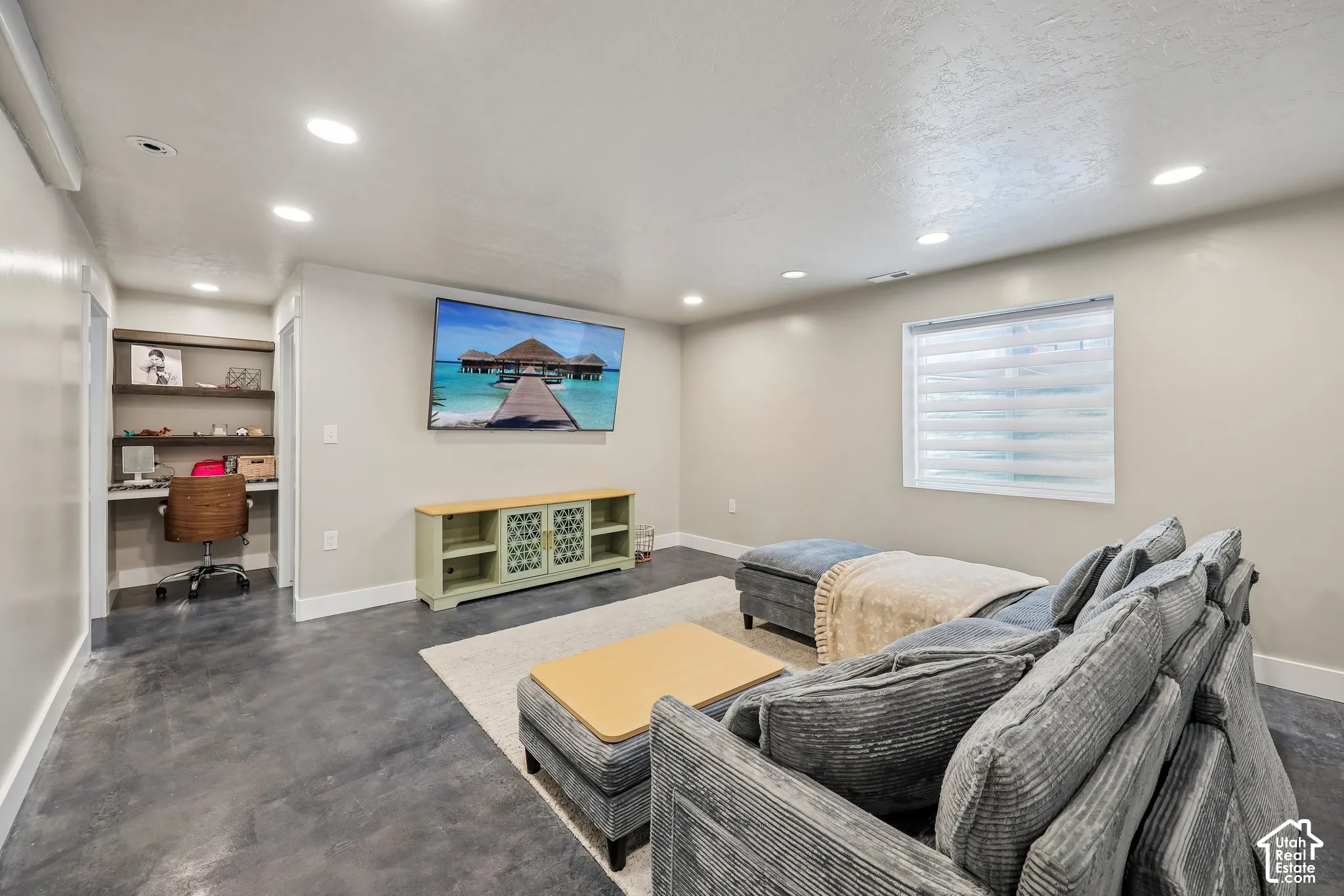 Recessed lighting, built-in desk with shelving, window with blinds, and concrete-finish flooring