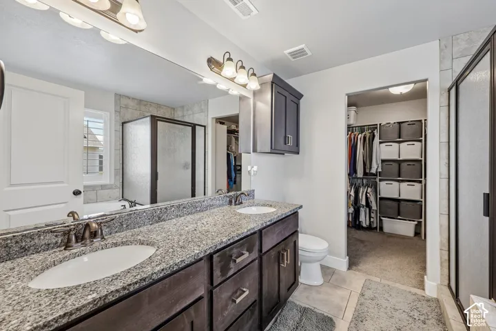 Dual vanity with granite countertop, tiled shower enclosure, separate toilet, built-in storage cabinetry, and an adjacent walk-in closet