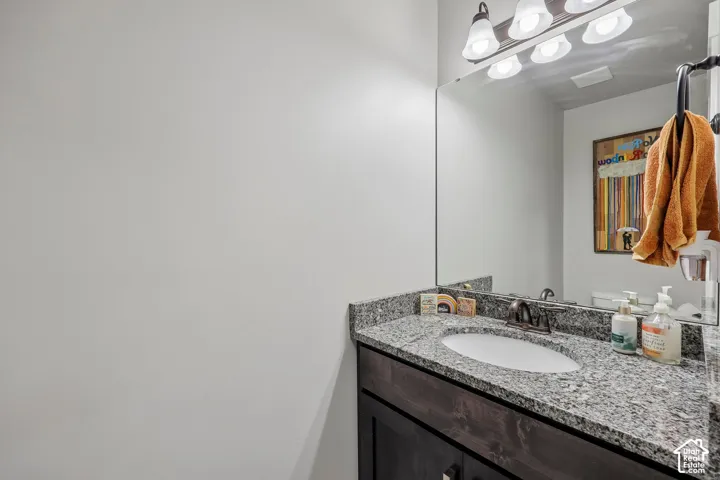 Granite-finish countertop with an undermount sink, dark wood-finish vanity, and a vanity mirror with overhead lighting