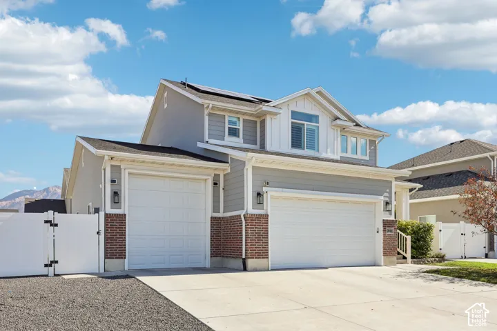 Two-story residence featuring light gray siding with brick accents, multiple garage doors, and solar panels