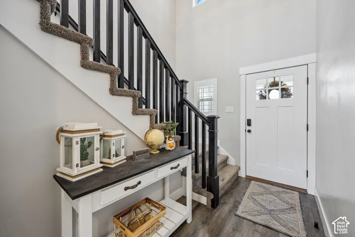 Hardwood-look flooring, white paneled entry door with glass inserts, white framed window, contemporary black balusters, and white console table with dark wood top