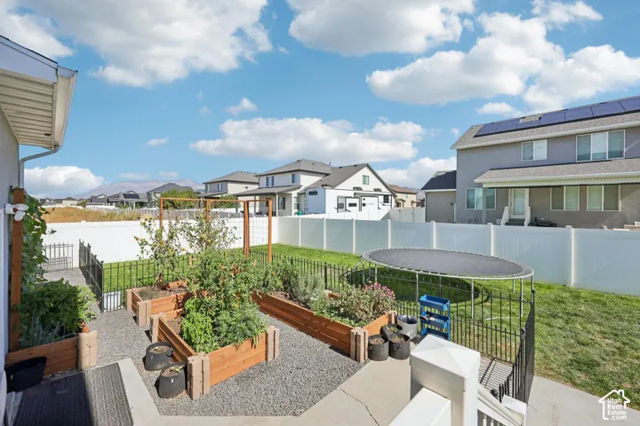 Backyard featuring elevated garden beds, gravel pathways, a manicured lawn, and a white vinyl privacy fence