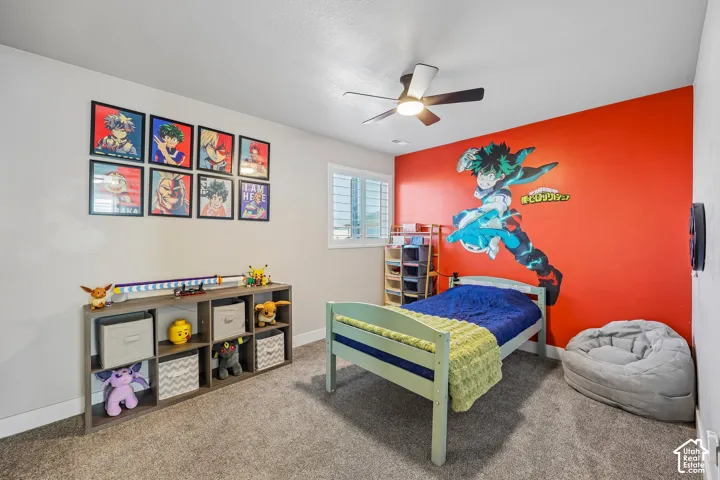 Recessed window with white blinds, ceiling fan with integrated lighting, wood-finish shelving unit, carpeted flooring, and a brightly painted accent wall