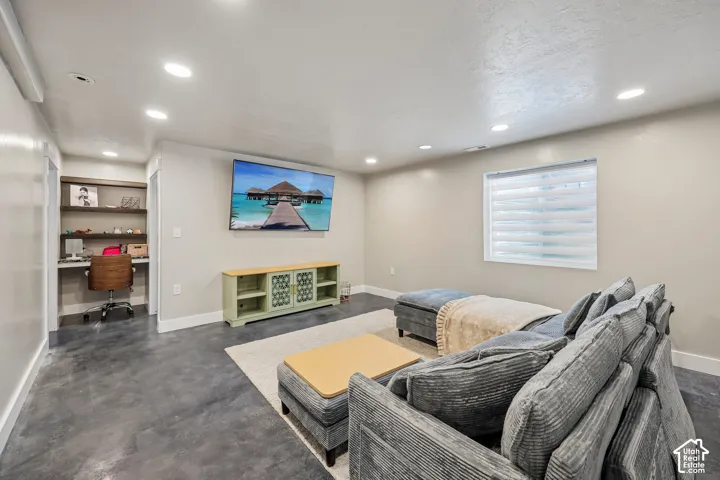 Recessed lighting, built-in desk with shelving, window with blinds, and concrete-finish flooring
